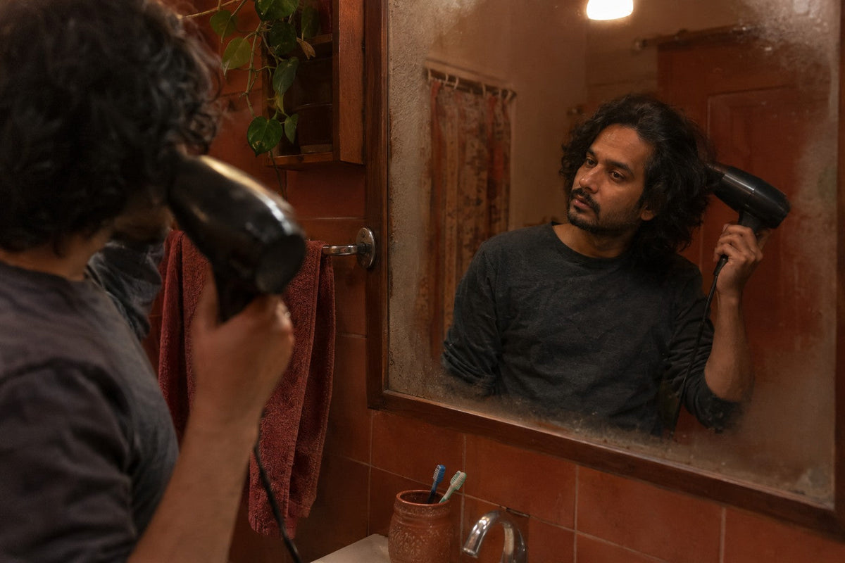 Man blow-drying his shoulder-length wavy hair at a bathroom mirror